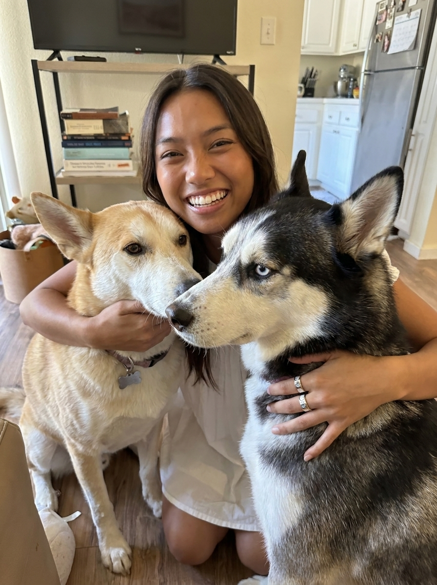 A smiling woman embracing her two dogs at home while wearing custom rings
